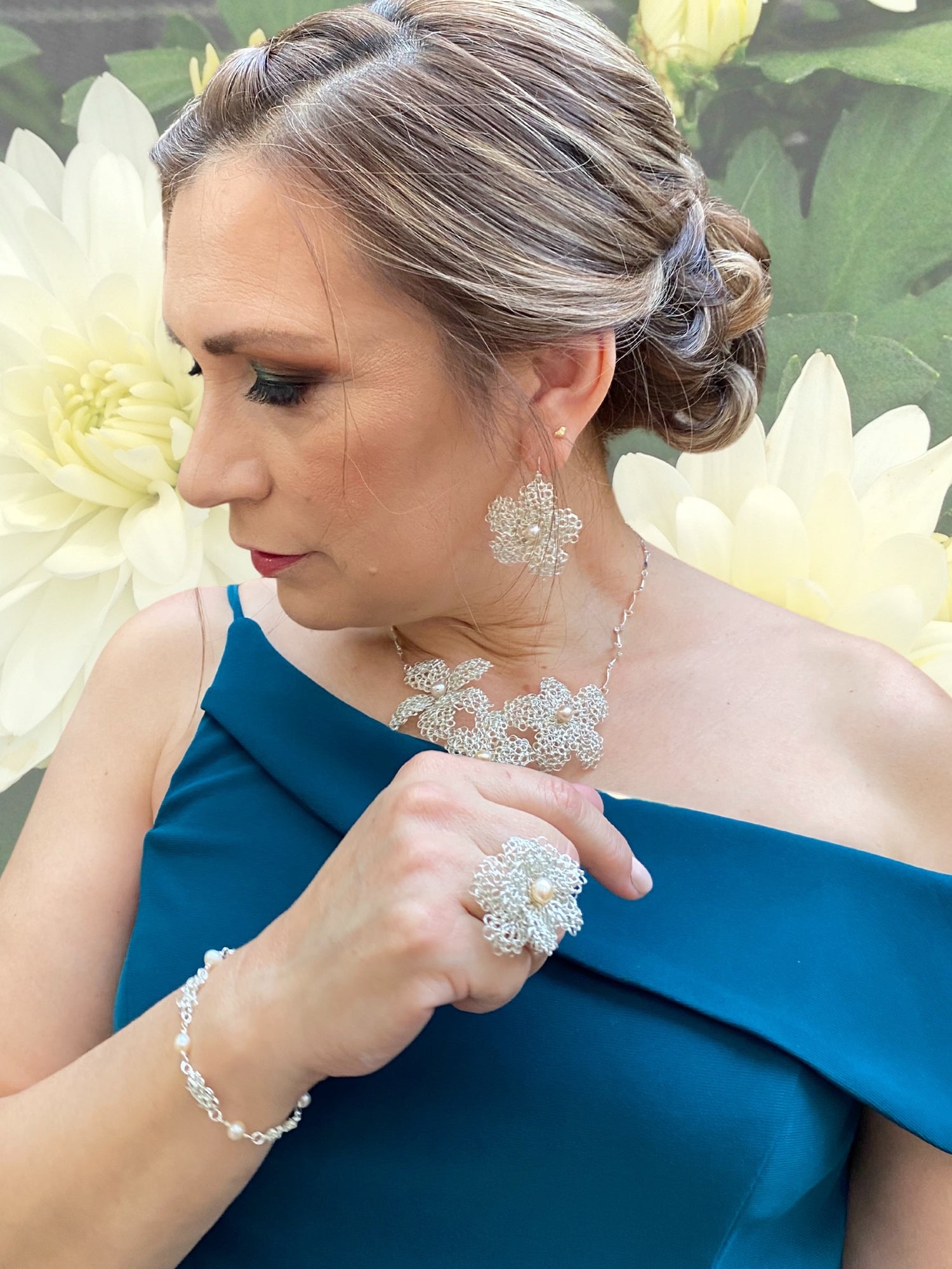 side profile of Any with her hair up while she wears a blue green dress and a silver flower shaped crochet jewelry collection